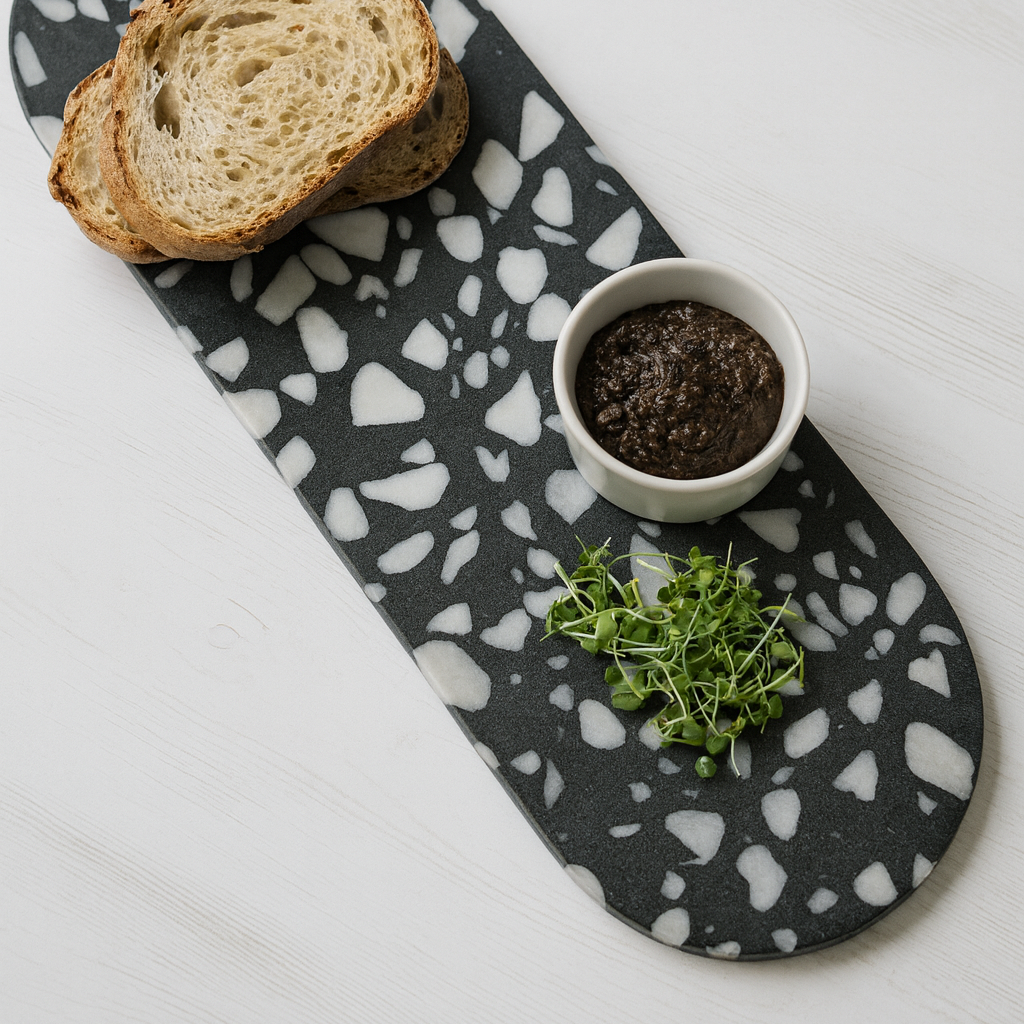 Black and white patterned tray with bread slices, a small bowl of spread, and fresh herbs on a light gray background.