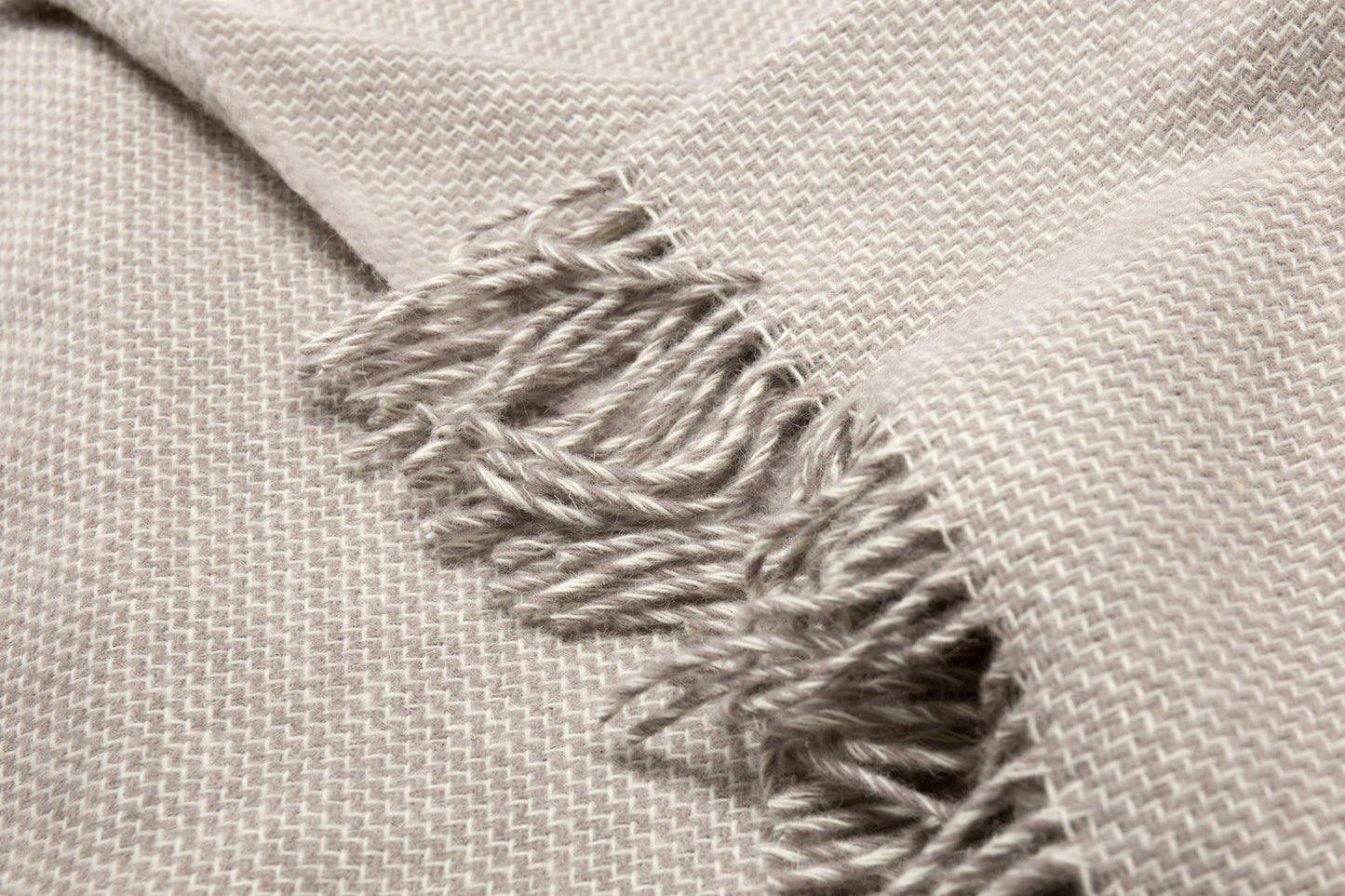 Close-up of a textured silver throw rug with frayed edge on a light gray background