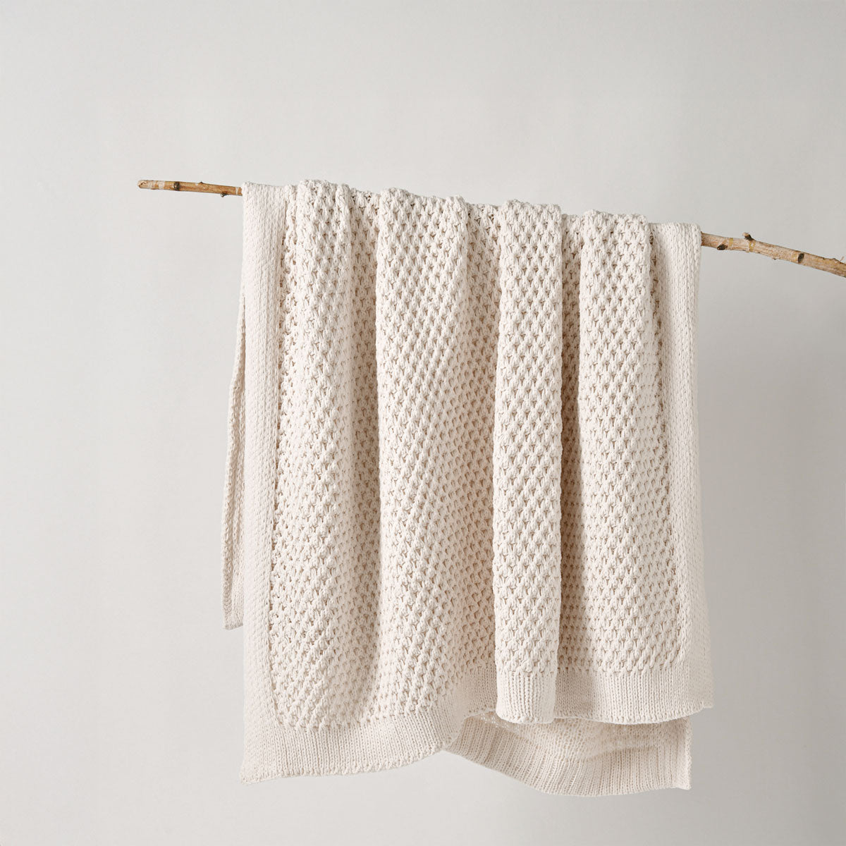 cream textured throw rug hanging on a wooden stick against a white background | Mirra Interiors