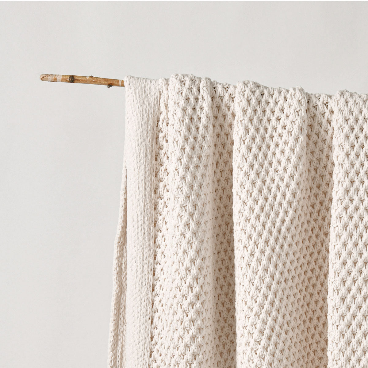 Knitted blanket draped over a wooden stick against a light gray background