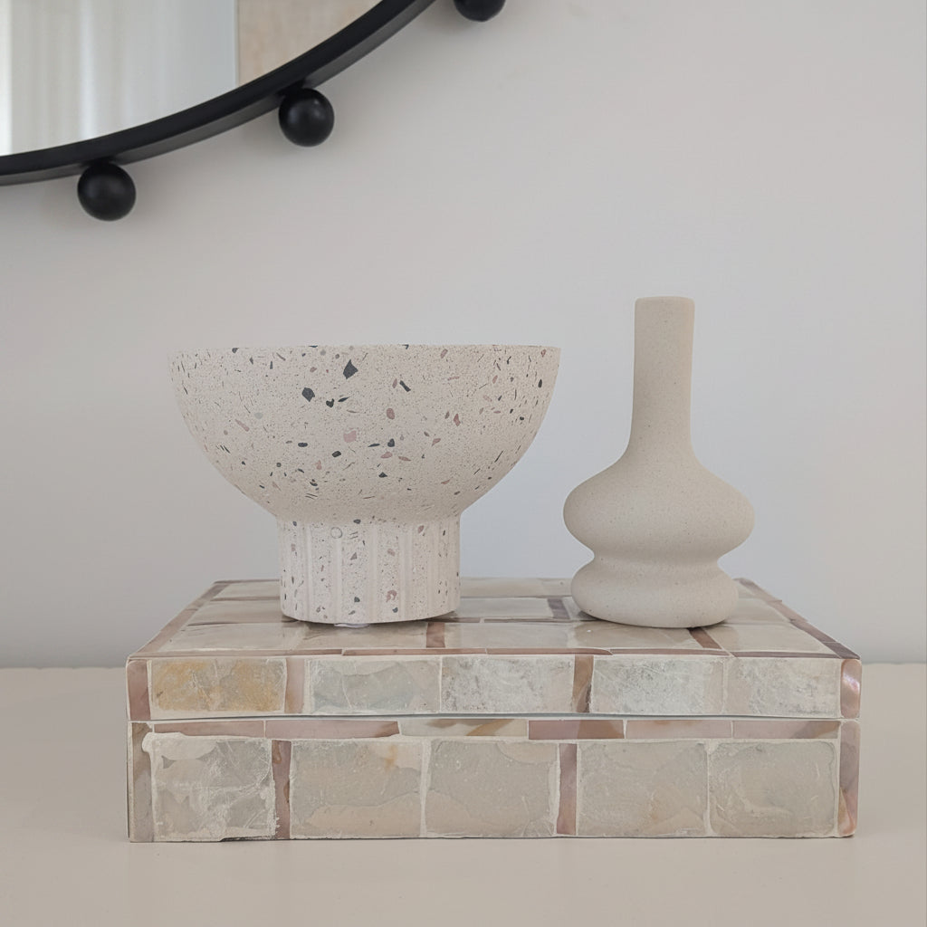 Terrazzo bowl on a decorative box with a black round mirror above on a white wall.