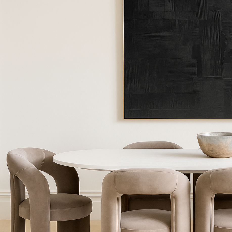 Dining room with a black abstract painting on the wall, white table, and beige velvet chairs.