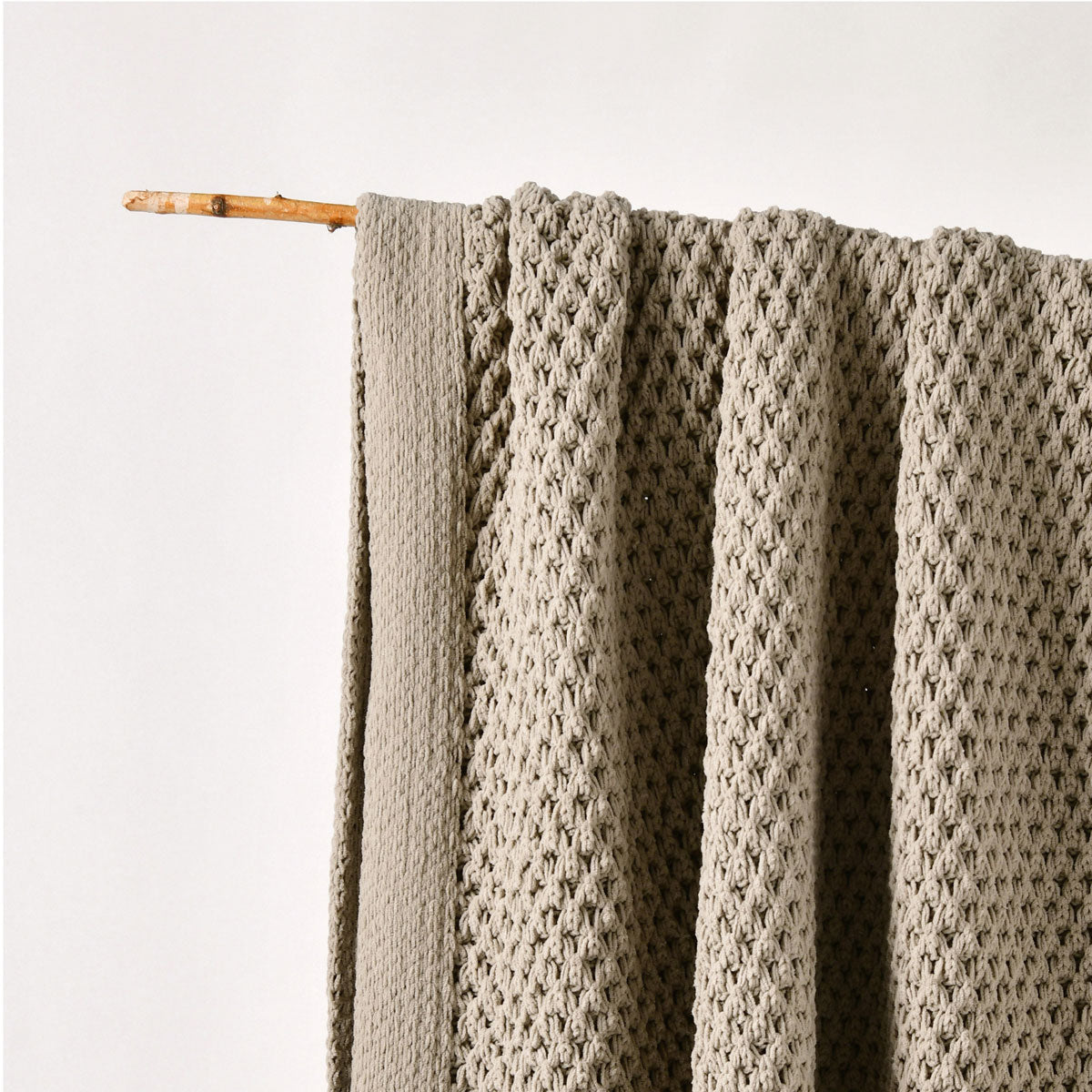 Knitted blanket draped over a wooden stick on a light background