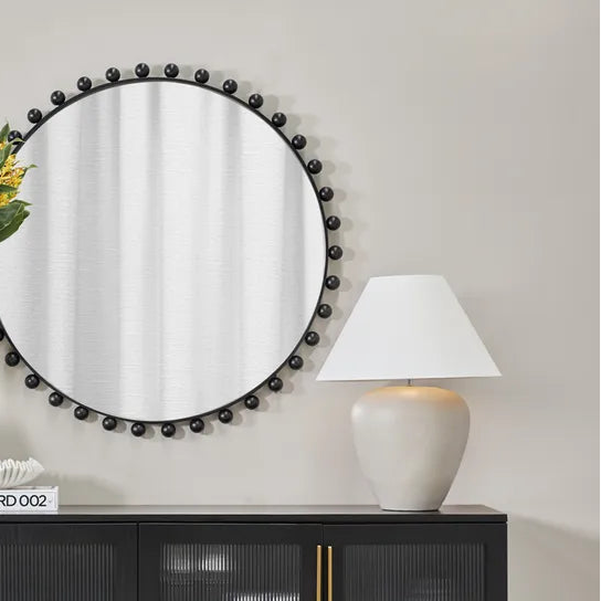 Modern interior with a black cabinet, round mirror, and decorative items.