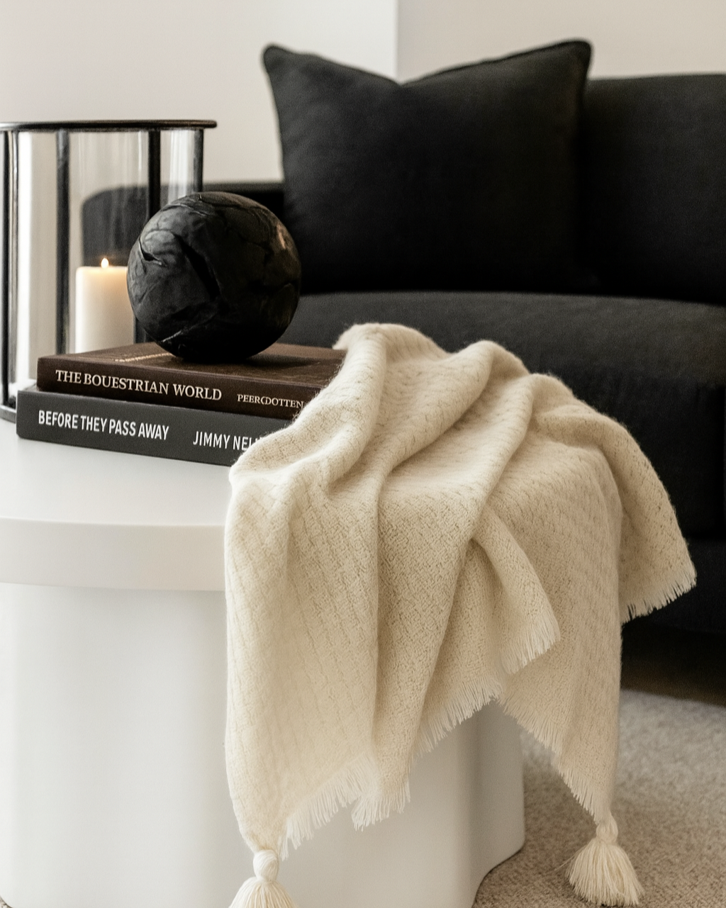 White side table with a beige blanket draped over it, next to a dark sofa with black pillows.