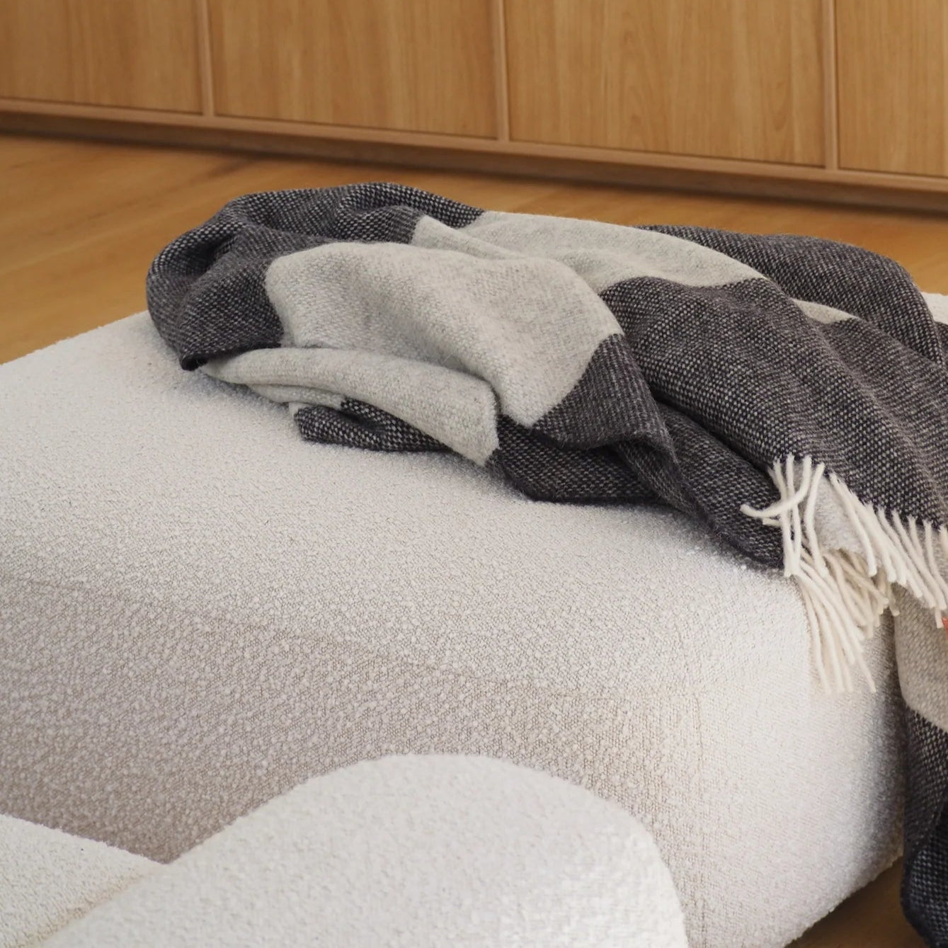 Plaid blanket draped over a white ottoman in front of a fireplace.