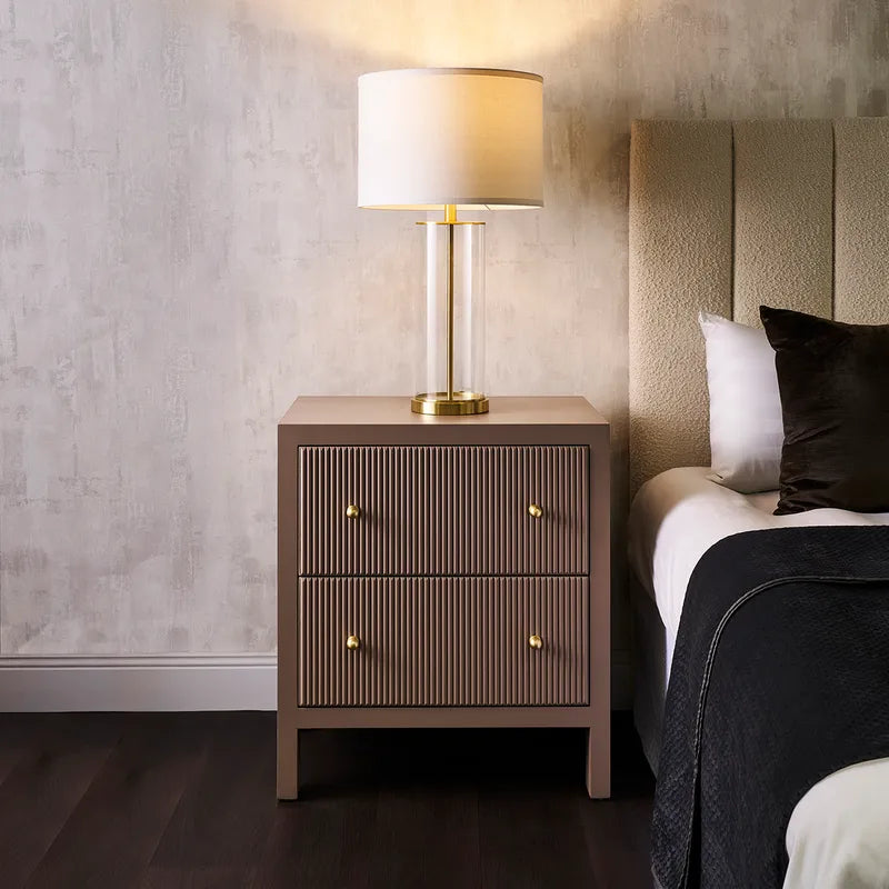 Bedroom with a nightstand and lamp next to a bed with pillows.