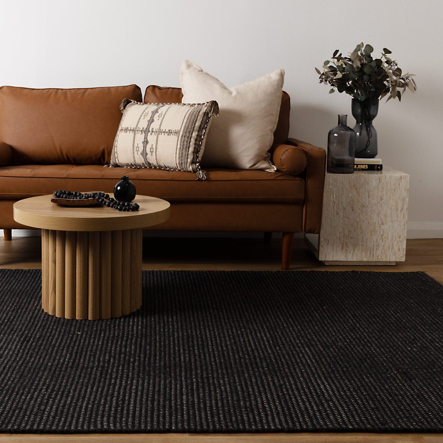 Brown sofa with decorative pillows, wooden coffee table, and side table with decor items in a living room setting.
