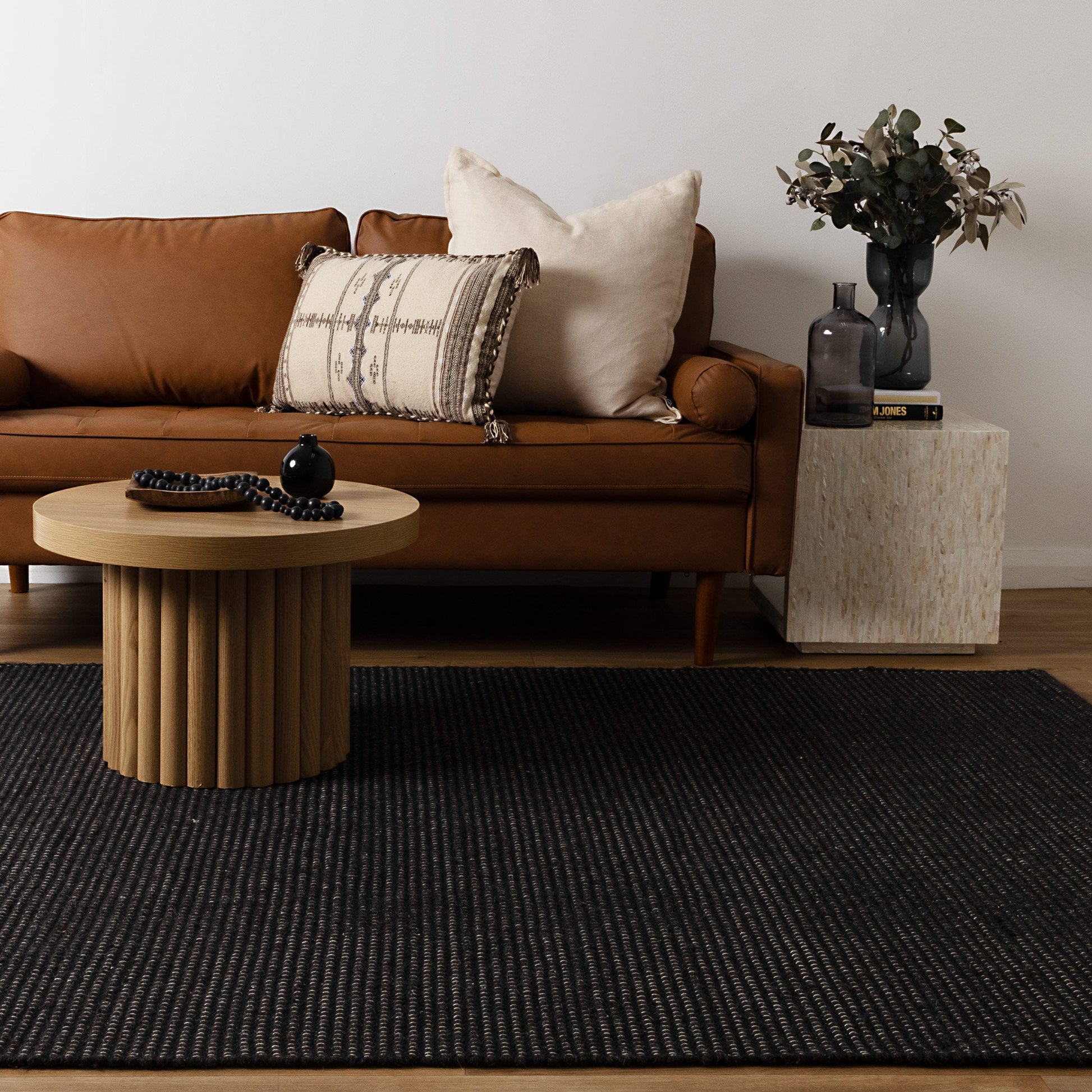 Brown sofa with decorative pillows, wooden coffee table, and side table with decor items in a living room setting.