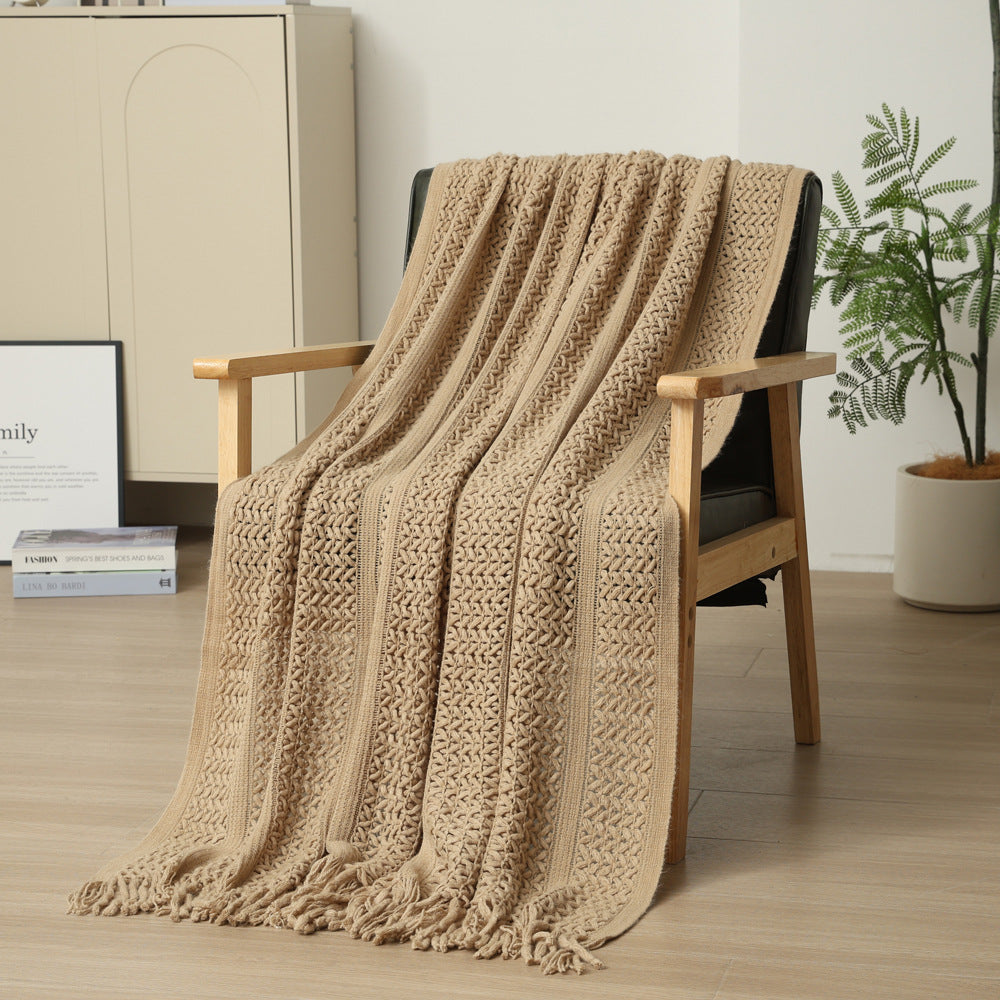 Beige knitted blanket draped over a wooden chair in a room with a plant and cabinet.