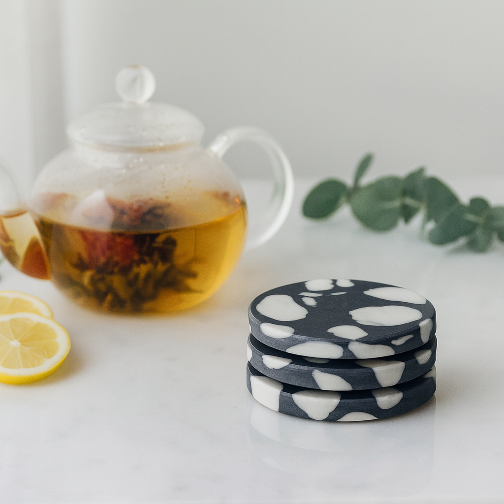 Tea set with teapot, lemon slices, and floral coasters on a white surface.