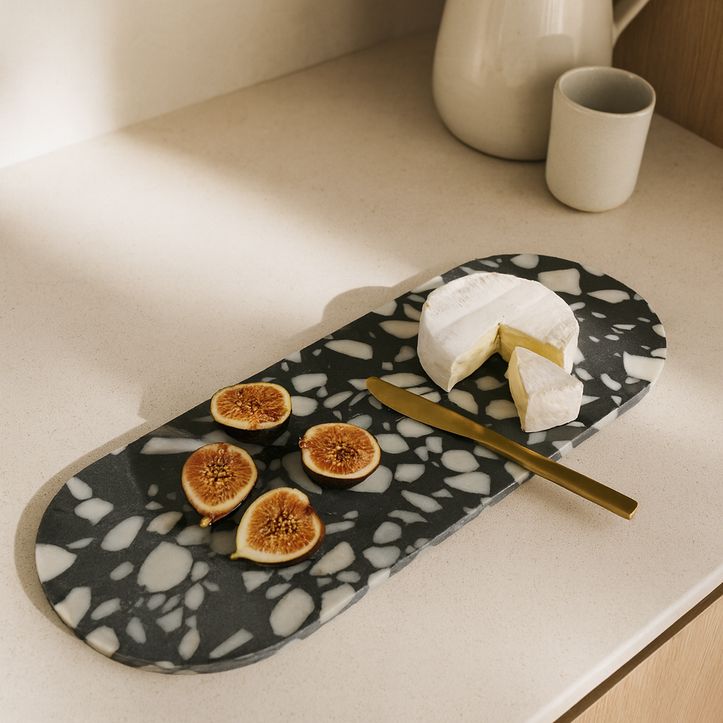 Black marble tray with figs, cheese, and a knife on a light countertop.