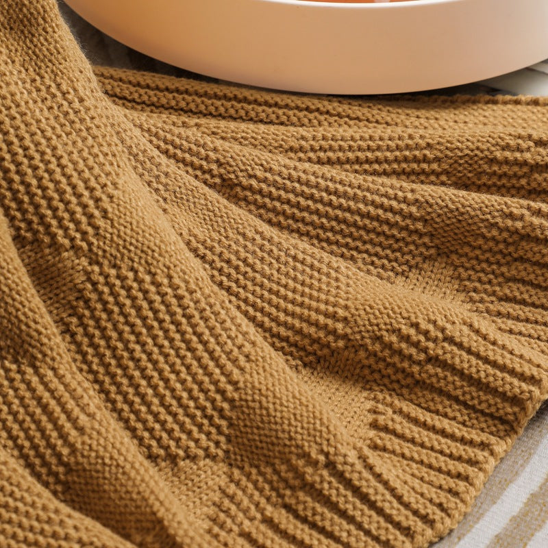 Brown knitted blanket draped over a surface with a blurred white object in the background