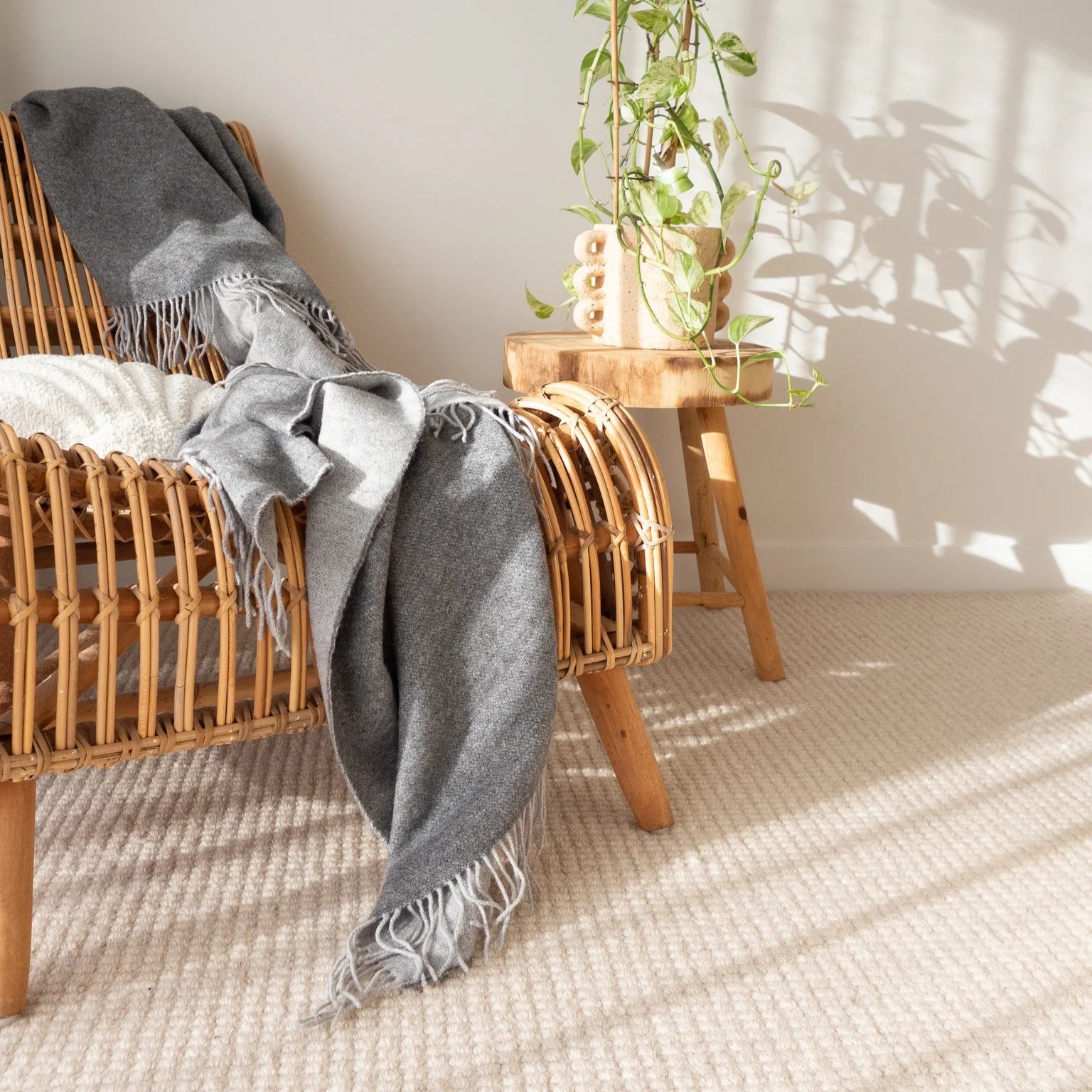 Wicker chair with a gray blanket and a small wooden table with plants in a bright room.