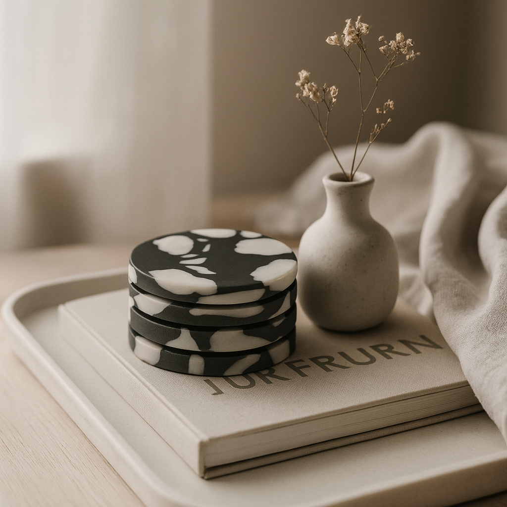 Stack of marble coasters on a book with a small vase containing dried flowers on a tray.