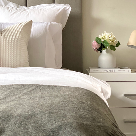 Neatly made bed with decorative pillows and a nightstand with a lamp and flowers.