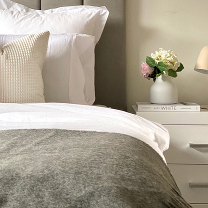 Neatly made bed with decorative pillows and a nightstand with a lamp and flowers.