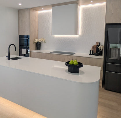 Modern kitchen with white island, black appliances, and light wood flooring.