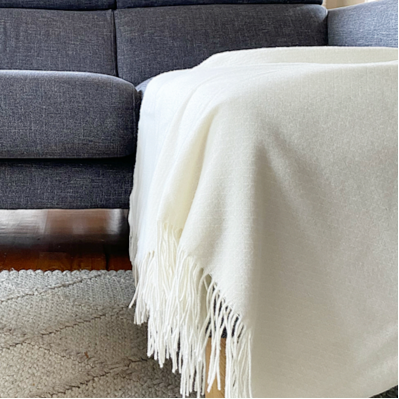 Gray sofa with a white blanket and wooden coffee table in a living room setting.