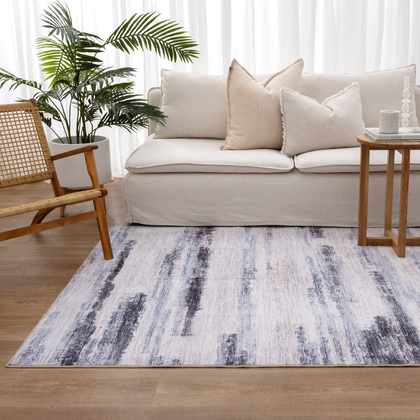 Living room with a patterned rug, beige sofa, wooden chair, and potted plant.