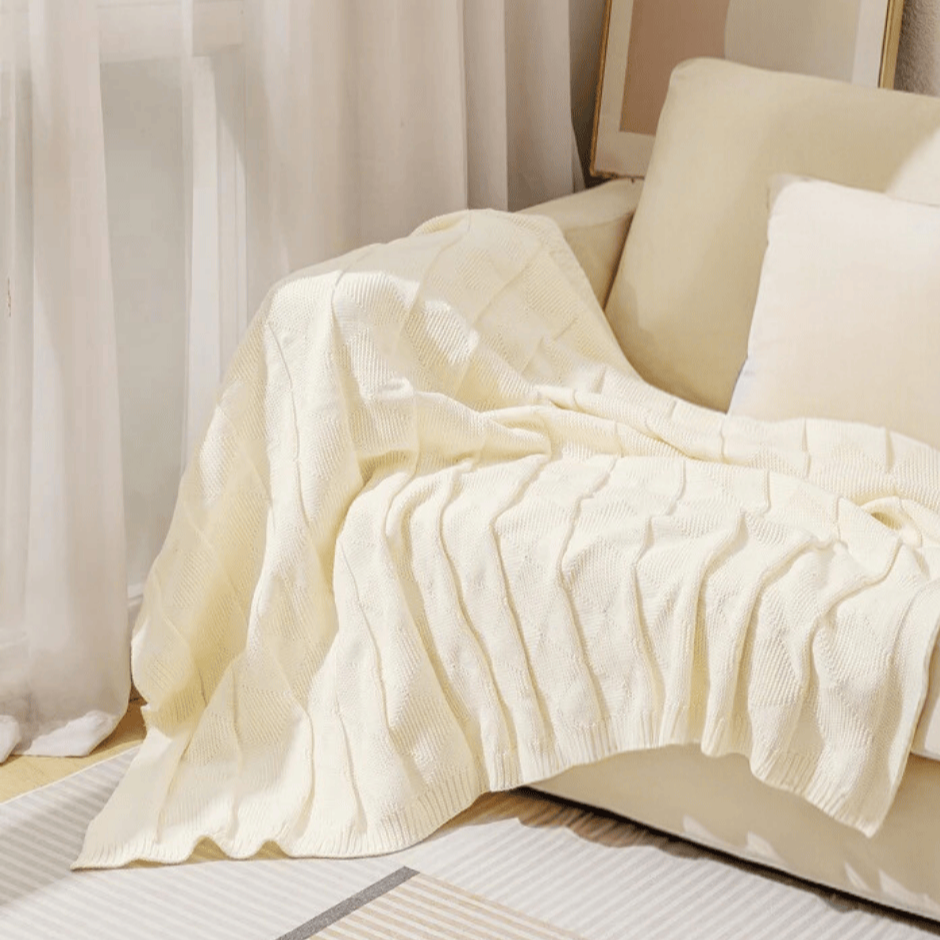 cream acrylic knit throw rug draped on creamy white sofa