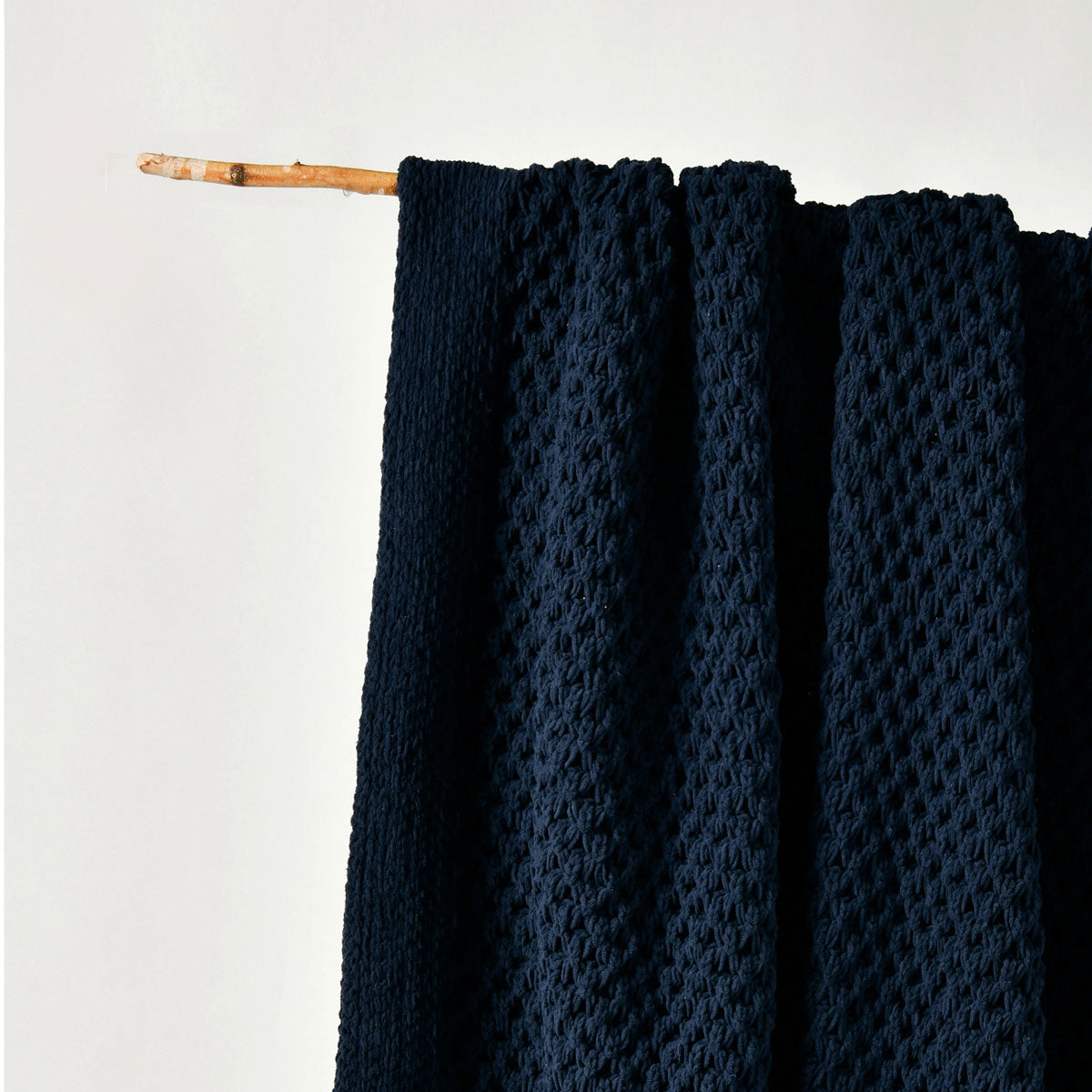 Dark blue textured fabric draped over a wooden stick on a light gray background