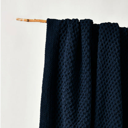 Dark blue textured fabric draped over a wooden stick on a light gray background