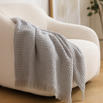 Gray textured blanket draped over a beige armchair in a home setting.