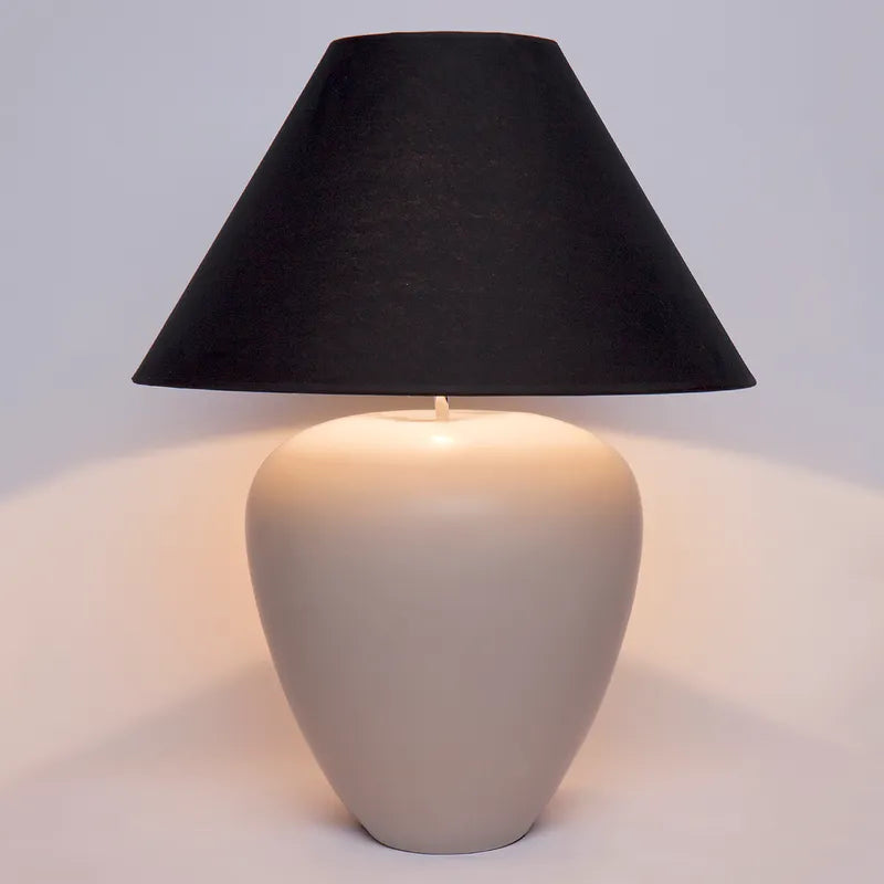 Table lamp with a black shade and beige base on a light gray background