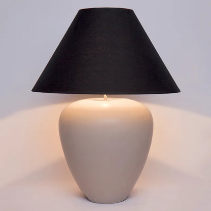 Table lamp with a black shade and beige base on a light gray background