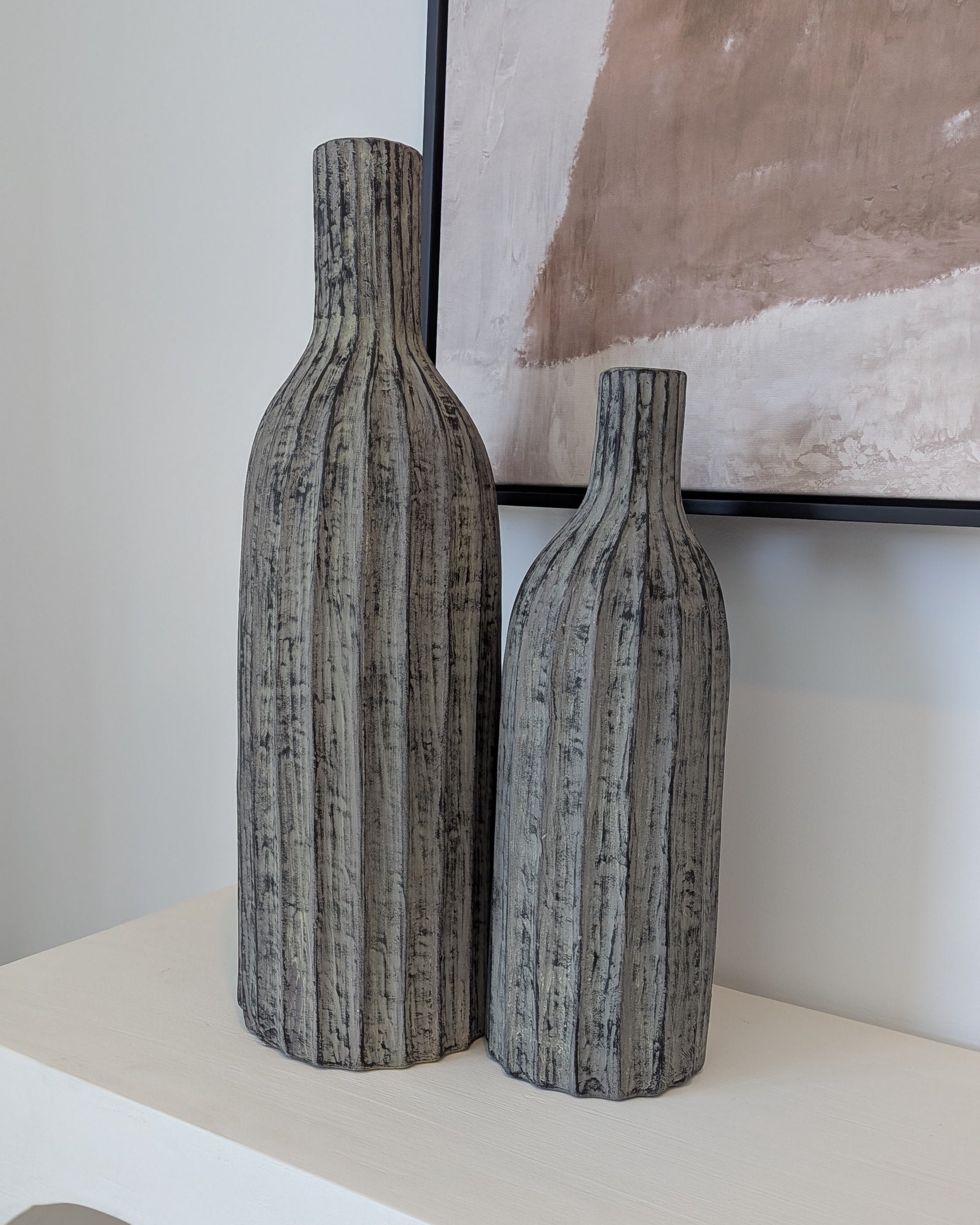 Two textured vases on a white console table with a framed abstract painting in the background.