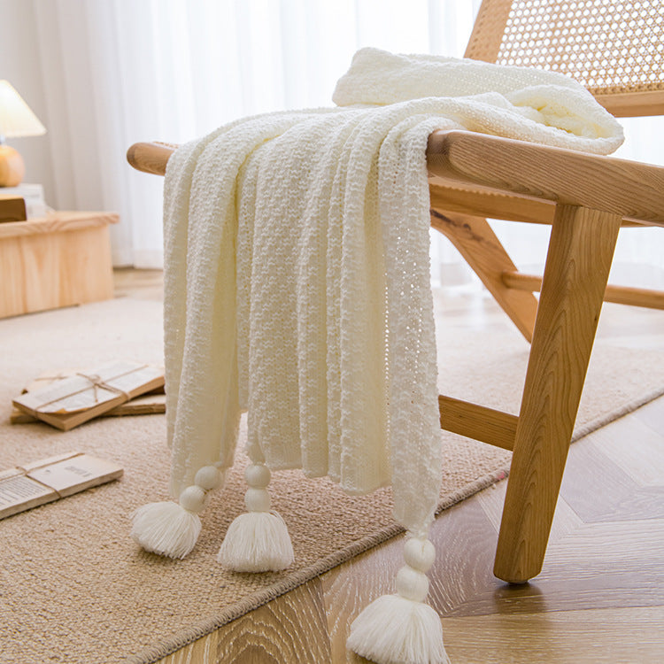 White textured blanket with tassels draped over a wooden chair in a bright room.