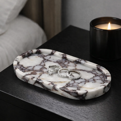 Marble-patterned tray with diamond rings on a black side table next to a lit candle.