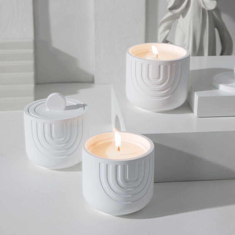 Three white ceramic candles with wicks on a light gray surface.