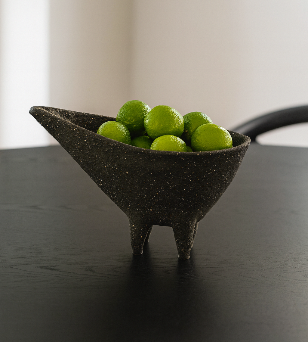 Black ceramic bowl with green limes on a dark table