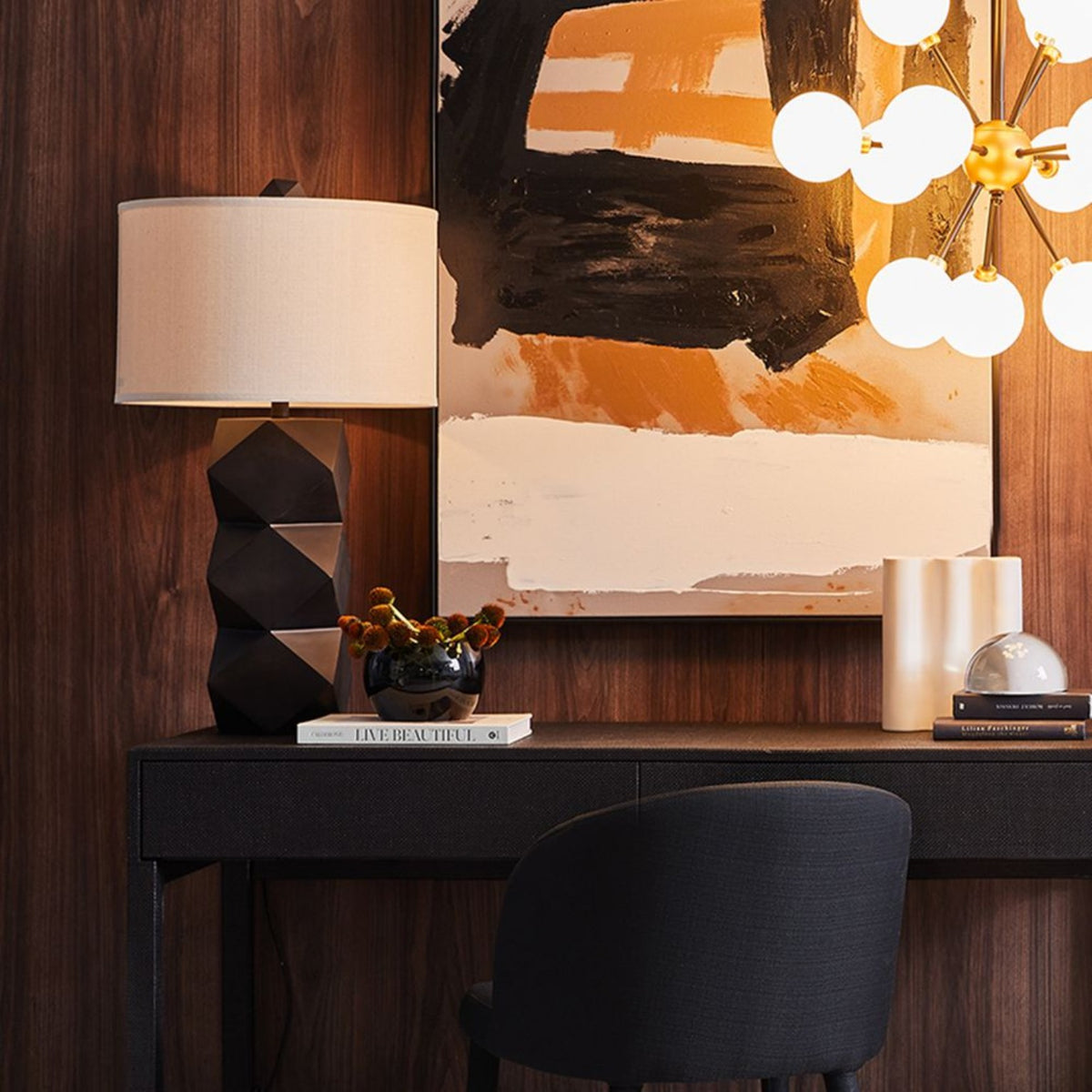 Bordeaux geometric table lamp with white shade styled on a dark console beneath abstract artwork