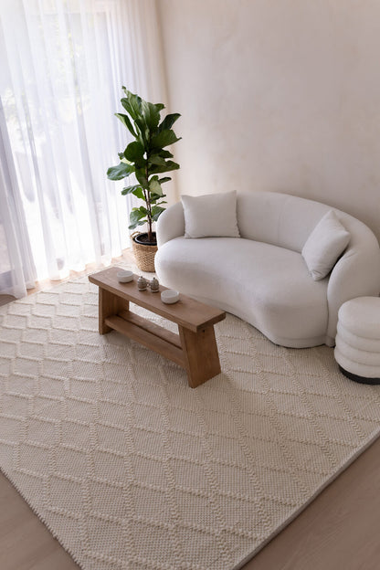 Modern living room with a white sofa, wooden coffee table, and a plant on a light-colored rug.