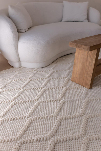 Beige rug with a diamond pattern in a living room setting with a white sofa and wooden coffee table.