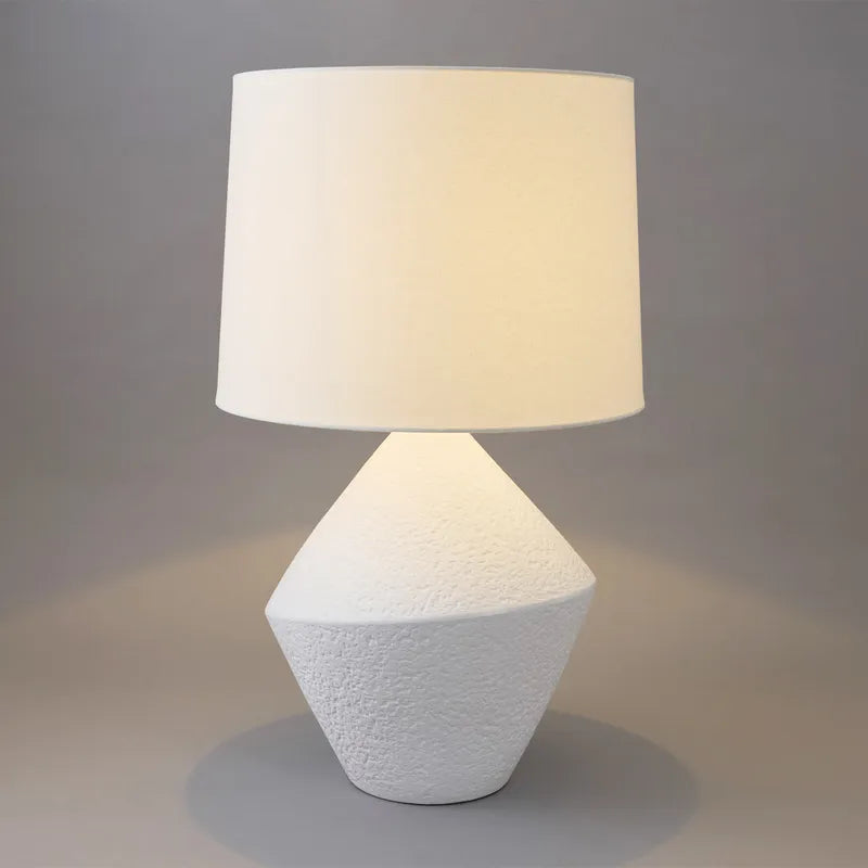 Table lamp with textured white base and beige shade on a neutral background
