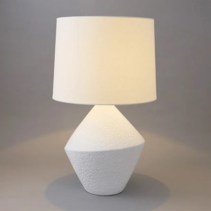 Table lamp with textured white base and beige shade on a neutral background